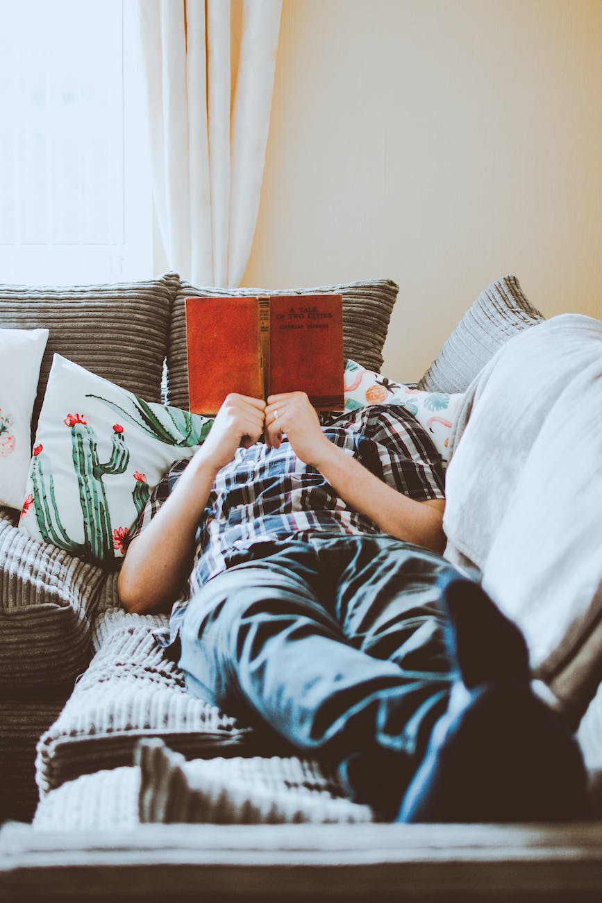 photo of man lying on bed while reading book